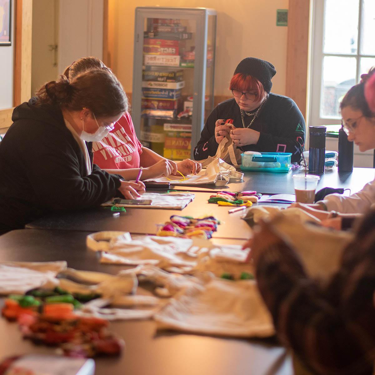 A group of students seated around a table, working on a craft with tote bags